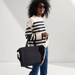 The Classic Tote in Black Sand, carried by its top handles by a model, shown from side.